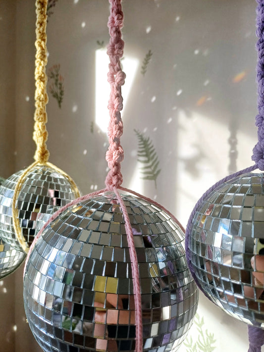 Disco balls with a macrame flower daisy chain patter. There are 3 colour macrame hangers, yellow, pink and purple.